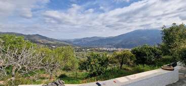 This image showcases a beautiful mountainous landscape with lush greenery, trees, and a distant village. The sky is partly cloudy, creating a peaceful and scenic atmosphere.