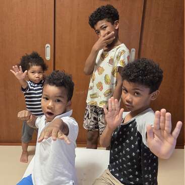 Quatre jeunes garçons aux cheveux bouclés prennent ensemble des poses ludiques d'arts martiaux à l'intérieur, devant des portes en bois, en regardant la caméra avec confiance et en faisant des gestes expressifs.