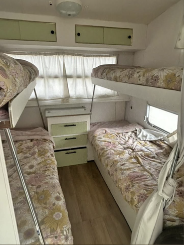 Dieses gemütliche Wohnmobilzimmer verfügt über vier Etagenbetten mit Bettwäsche mit Blumenmuster, Holzboden, Hängeschränke, eine kleine Kommode und Vorhänge, die sanftes Tageslicht hereinlassen.