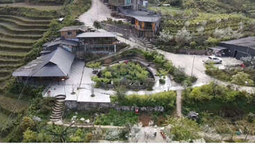 This image shows a scenic hillside property with modern buildings, terraced gardens, winding stone steps, lush greenery, flower trees, and paved walkways surrounding the area.