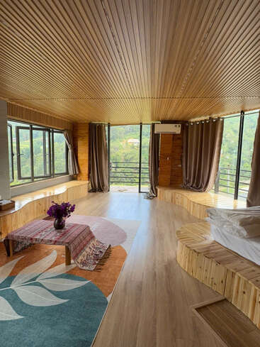 Este quarto espaçoso e aconchegante tem paredes e teto revestidos de painéis de madeira, janelas amplas com vistas panorâmicas, uma mesa baixa com flores, tapetes em tons terrosos e assentos embutidos.