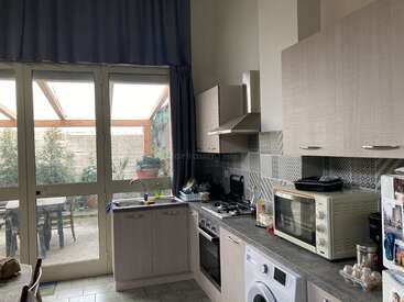 L'image montre une cuisine moderne avec des placards clairs, une porte vitrée menant à un patio et une gamme d'appareils électroménagers comprenant une cuisinière, un four et un four à micro-ondes.