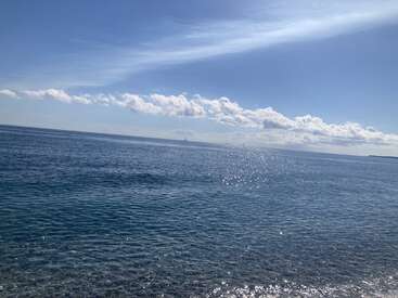 L'image représente une étendue d'eau sereine avec de douces ondulations, sur fond de ciel bleu avec des nuages blancs et une ligne d'horizon lointaine.