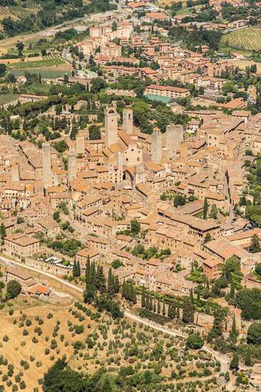 The image depicts an aerial view of a small town with numerous buildings, trees, and a road, showcasing a charming and historic European-style village.