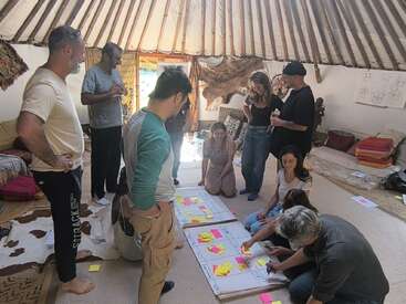 A group of people collaborate in a cozy, round room, brainstorming ideas with colorful sticky notes on large paper sheets, fostering teamwork and creativity in a relaxed environment.