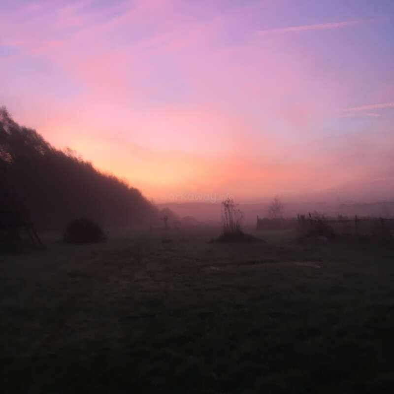 L'image représente un paysage serein au lever ou au coucher du soleil, avec un ciel vibrant aux teintes roses et violettes, sur un fond sombre.