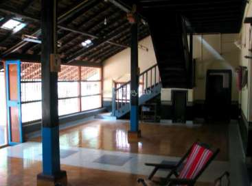 Das Bild zeigt einen geräumigen Raum mit einer Treppe, einem rot-weiß gestreiften Stuhl, Holzböden und einer hohen Decke mit sichtbaren Balken und Oberlichtern.