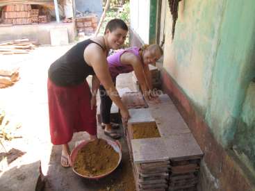 Das Bild zeigt zwei Frauen, die mit einem Gemisch aus Erde und Sand arbeiten, wahrscheinlich bei einem Bauvorhaben oder einem Bauprojekt.