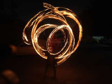 Une personne exécute une danse du feu hypnotique la nuit, créant des motifs tourbillonnants complexes de lumière avec des traînées flamboyantes, illuminant l'obscurité avec des mouvements circulaires enflammés.