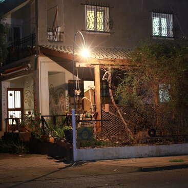L'image représente un bâtiment de deux étages avec un balcon et un jardin, avec un lampadaire et une clôture, illuminés la nuit.