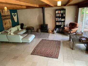 This cozy living room features a sectional sofa, patterned rugs, a wood stove, bookshelf, armchair, rustic table, wall hangings, and sliding glass doors to outside.