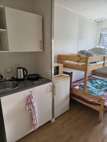 Esta habitación pequeña y práctica cuenta con una cocina americana compacta con fregadero, hervidor y mininevera, además de una litera de madera y una ventana que deja pasar la luz natural.