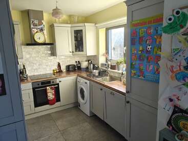 This cozy kitchen features white cabinets, a washing machine, and an oven. Children's artwork and an alphabet poster decorate the fridge. Natural light fills the room.