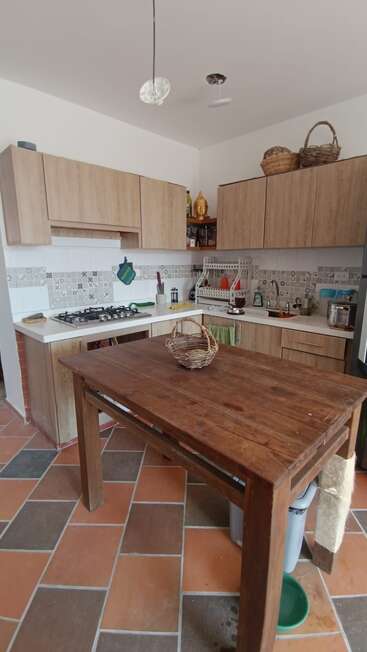 This image shows a cozy kitchen with wood cabinets, patterned tile backsplash, a gas stove, and a wooden table featuring a woven basket centerpiece on top.