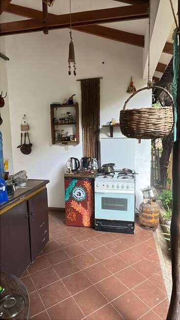 Dieses Bild zeigt eine rustikale Küche mit Gasherd, Wasserkocher, Utensilien, offenen Regalen, hängendem Weidenkorb, Holzbalken und einem gemütlichen, natürlichen Ambiente.