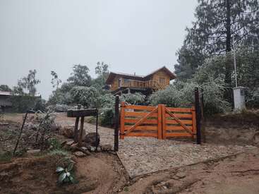Eine gemütliche Holzhütte liegt auf einem Hügel, umgeben von frostigen Bäumen. Ein Steinpfad führt zu einem hellen Holztor, das eine friedliche Winterszene heraufbeschwört.