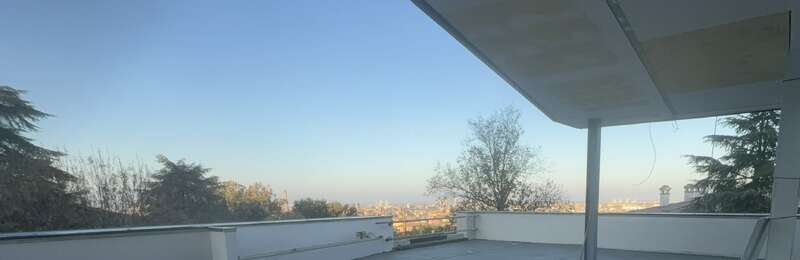 La imagen muestra un tejado con barandillas, un árbol a la derecha y el perfil de la ciudad al fondo, bajo un cielo azul despejado.
