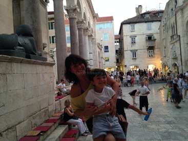 The image depicts a woman and a child posing for a photo on a stone street, surrounded by people and buildings, with a watermark reading \'workaway\' in the center.