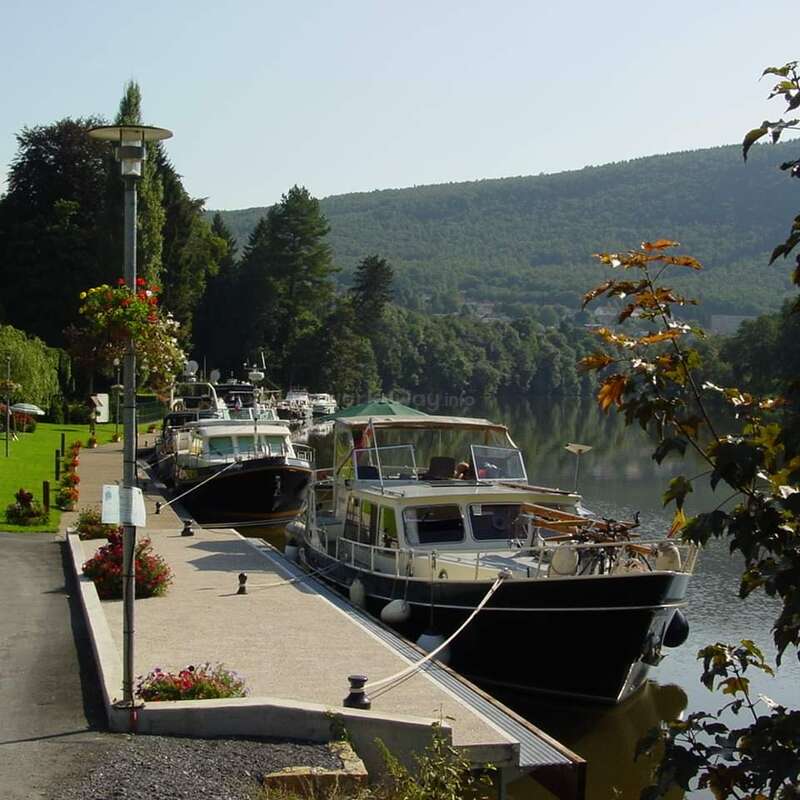 The image depicts a serene scene of boats docked at a marina, surrounded by lush trees and a picturesque landscape under a clear blue sky.