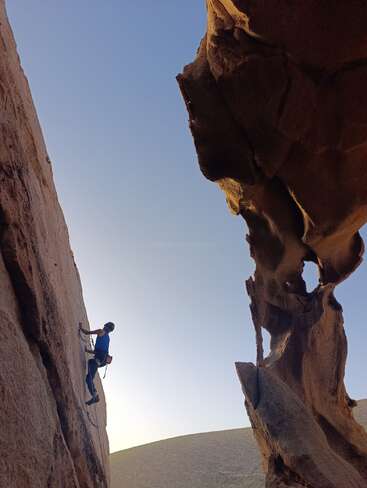 A rock climber ascends a vertical cliff, surrounded by dramatic rock formations and clear blue sky, epitomizing adventure, determination, and the beauty of outdoor exploration.