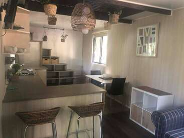 This cozy kitchen and dining area features wicker lighting, wooden countertops, a small dining table, modern shelving, plants, and a "LIVE BEAUTIFULLY" framed wall art.