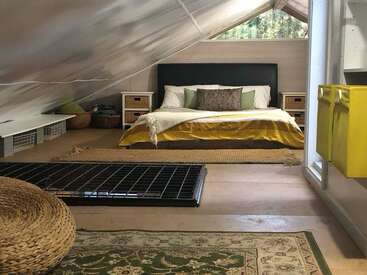 This cozy attic bedroom has a sloped ceiling, a large bed with yellow bedding, side tables, baskets, woven mats, a rug, and a bright yellow cabinet.