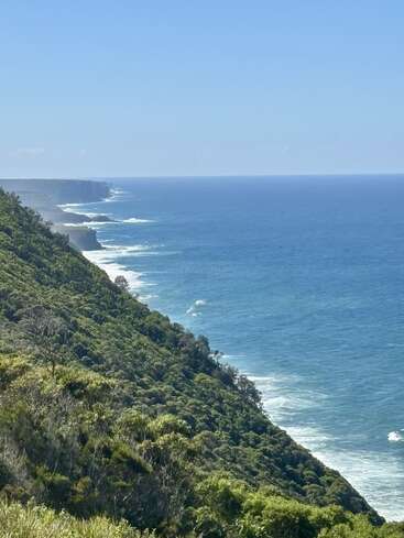 Uma paisagem costeira de tirar o fôlego, com penhascos verdes e escarpados que descem abruptamente até o oceano azul profundo, com as ondas quebrando na costa sob um céu limpo.