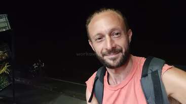 La imagen muestra a una persona con pelo corto y camisa blanca, posando para una foto. Están de pie delante de un fondo liso, posiblemente para una sesión de modelaje o moda.