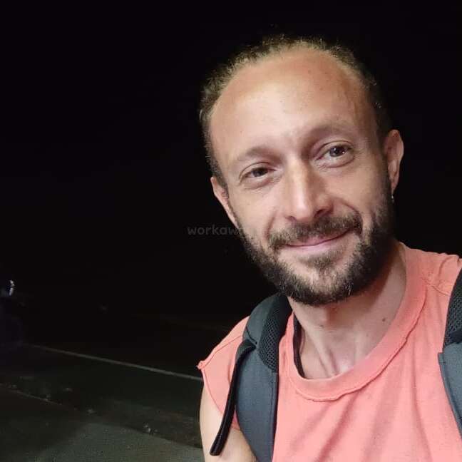 Das Bild zeigt eine Person mit kurzen Haaren und einem weißen Hemd, die für ein Foto posiert. Sie steht vor einem schlichten Hintergrund, möglicherweise für ein Model- oder Modeshooting.