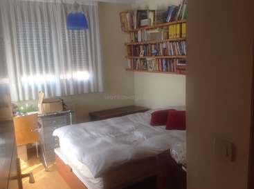 A imagem mostra um quarto aconchegante com uma cama, estante, escrivaninha e janela, com cortinas brancas e uma lâmpada azul, exalando uma atmosfera calorosa e convidativa.
