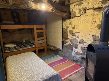 Une chambre rustique et chaleureuse avec des murs en pierre, un plafond aux poutres apparentes, des lits superposés, un lit simple, des tapis colorés et un poêle à bois pour se réchauffer.