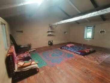 Cette chambre simple et rustique est dotée d'un plancher en bois, d'un matelas au sol, de tapis colorés, d'un mobilier minimal, d'une petite fenêtre et de quelques étagères murales. Ambiance chaleureuse.