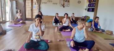 Eine Gruppe von Frauen sitzt mit gekreuzten Beinen auf Yogamatten in einem hellen Studio und übt gemeinsam Atemübungen mit abwechselnden Nasenlöchern, wodurch eine ruhige, konzentrierte und friedliche Atmosphäre entsteht.