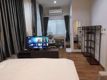 Um quarto moderno e arrumado tem cama, TV com serviços de streaming, mesa com cadeira de escritório, estante, janela grande com cortinas, piso de madeira e espelho.