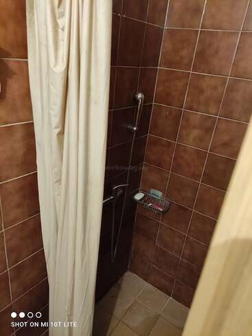 Auf diesem Bild ist ein kleiner Duschbereich zu sehen, mit braun gefliesten Wänden, einem cremefarbenen Duschvorhang, einer Handbrause, einem Haltegriff, einer Seifenschale und einem Stück Seife.