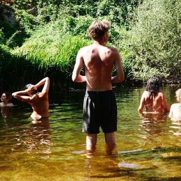 Un groupe de personnes nage et se détend dans un étang naturel entouré d'une végétation luxuriante, profitant du soleil et de l'atmosphère paisible d'une journée d'été.
