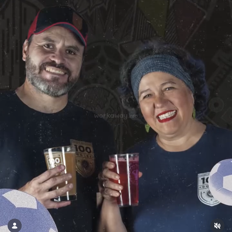 Un hombre y una mujer sonrientes sostienen bebidas y posan juntos, vistiendo camisetas a juego con el número «100». El fondo es oscuro y decorativo, lo que crea un ambiente alegre y festivo.