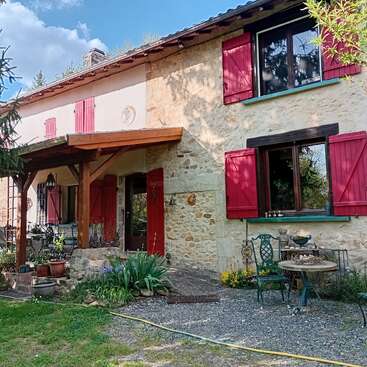 Esta encantadora casita de piedra cuenta con contraventanas rojas, un porche de madera, muebles de jardín y plantas de vivos colores. Luminosa y acogedora, está rodeada de vegetación y de un ambiente tranquilo.