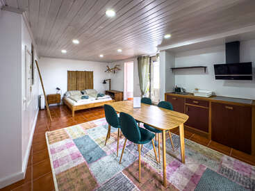 Ce studio confortable dispose d'une chambre et d'une kitchenette modernes, d'une table à manger en bois avec des chaises sarcelles, d'un tapis en patchwork, d'un sol carrelé et d'une décoration rustique, alliant confort et style.
