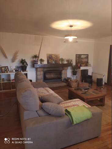 L'image représente un salon confortable avec une cheminée, des planchers en bois et un canapé gris, dans une atmosphère chaleureuse et accueillante.