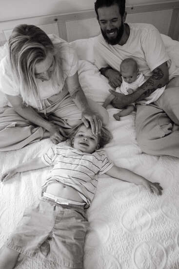 Um momento familiar alegre capturado em preto e branco: dois pais sentados em uma cama com seus filhos felizes, irradiando calor, amor e conexão.
