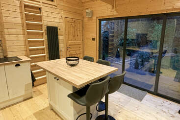 This cozy, modern cabin features wooden walls and floors, a kitchen island with barstools, a loft ladder, sliding glass doors, and a view of the outside patio.