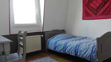 Das Bild zeigt einen Raum mit einem Bett, einem Schreibtisch und einem Stuhl sowie einem Fenster mit Blick auf ein Gewässer, wahrscheinlich ein Haus oder eine Wohnung.