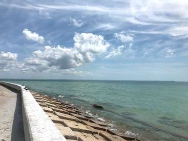 The image depicts a serene ocean scene with a concrete walkway, featuring a railing and stairs leading into the water, set against a blue sky with white clouds.