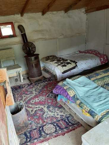 Das Bild zeigt ein rustikales Zimmer mit zwei Betten, einem Teppich und einem Holzofen, das eine gemütliche und alte Atmosphäre ausstrahlt.