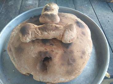 Das Bild zeigt ein großes, rundes Stück Teig mit einem Loch in der Mitte, das mit kleineren Teigstücken auf einem Metalltablett belegt ist.