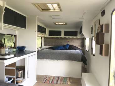A imagem mostra o interior de um pequeno trailer, com cama, cozinha e espaço de armazenamento, com foco na funcionalidade e no aconchego.