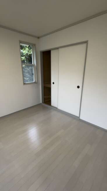 Dieses Bild zeigt einen einfachen, leeren Raum mit hellem Holzfußboden, einem kleinen Fenster und weißen Schrankschiebetüren. Der Raum wirkt sauber und gut beleuchtet.