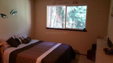 L'image représente une pièce avec une table et des chaises, dotée d'une grande fenêtre et d'une porte, avec un mur proéminent à l'arrière-plan. La pièce est bien éclairée et présente un aspect propre.