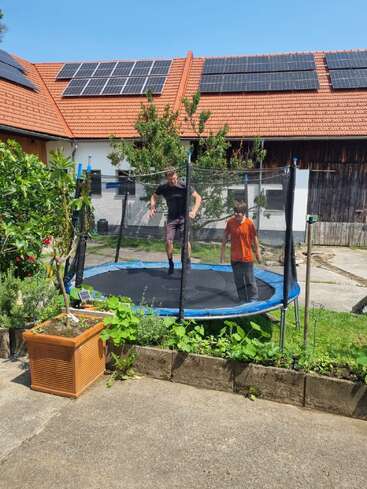 Ein Mann und ein Junge toben auf einem Trampolin in einem sonnigen Garten herum. Das Haus hinter ihnen hat Sonnenkollektoren auf dem Dach.
